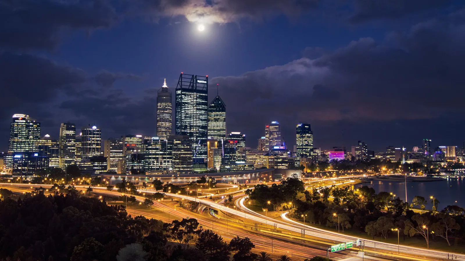 Illuminated city skyline and highway beneath the moon