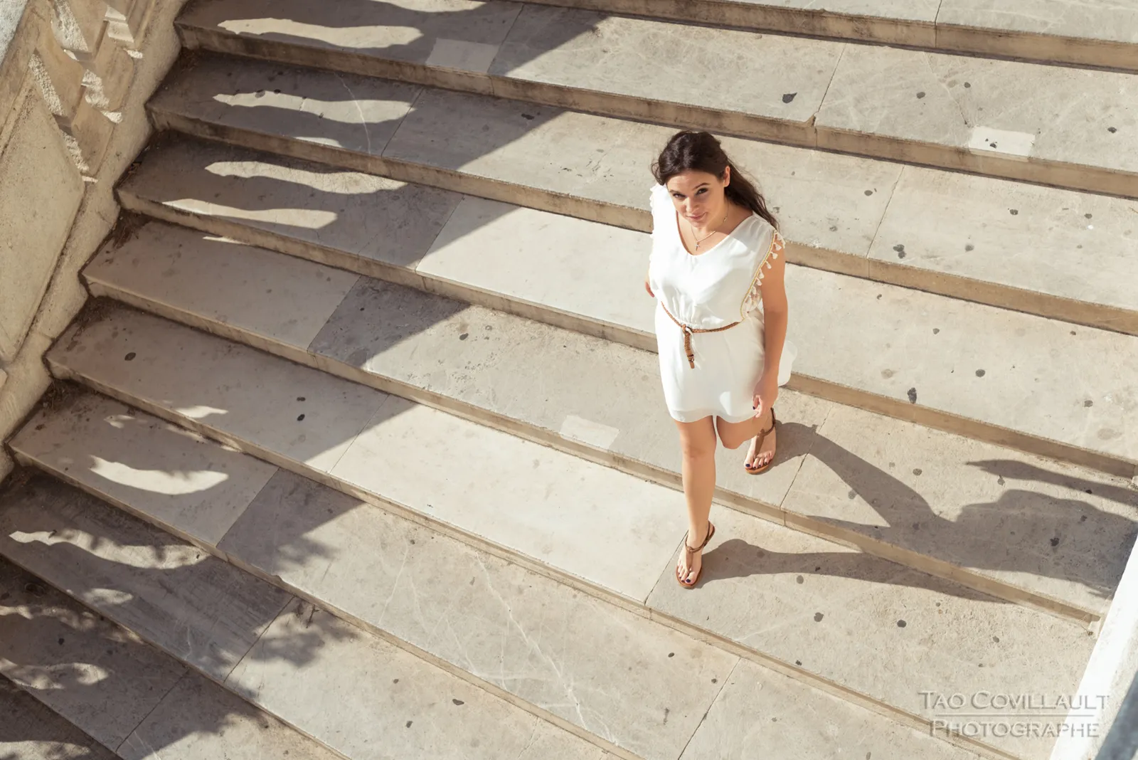 Woman in a white dress posing on stone steps and beside a balustrade.