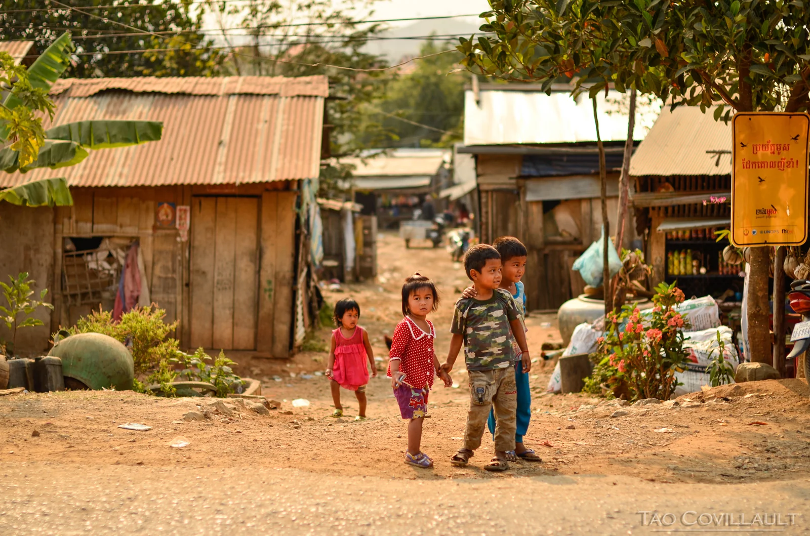 Children standing on a dusty path between village buildings.