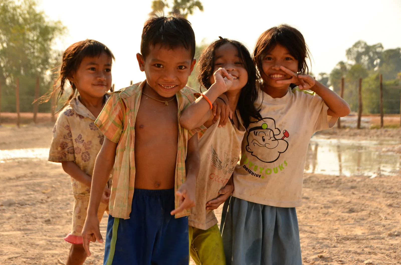Three children standing together beside a shallow pond.