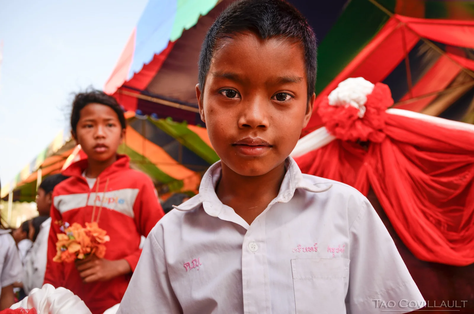 Child in a white shirt before colorful temple decorations in Cambodia.