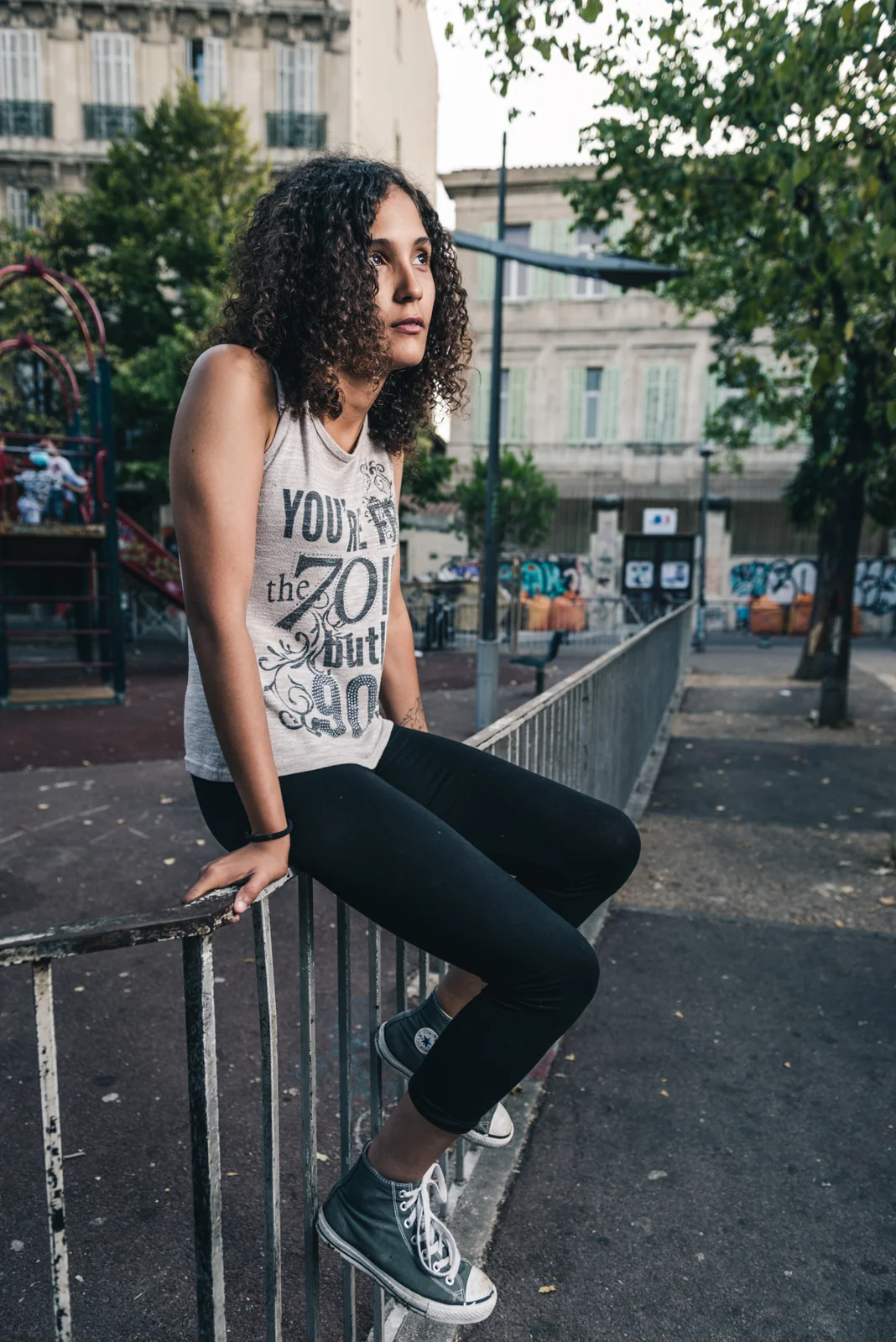 Woman seated sideways on a railing in a public square.