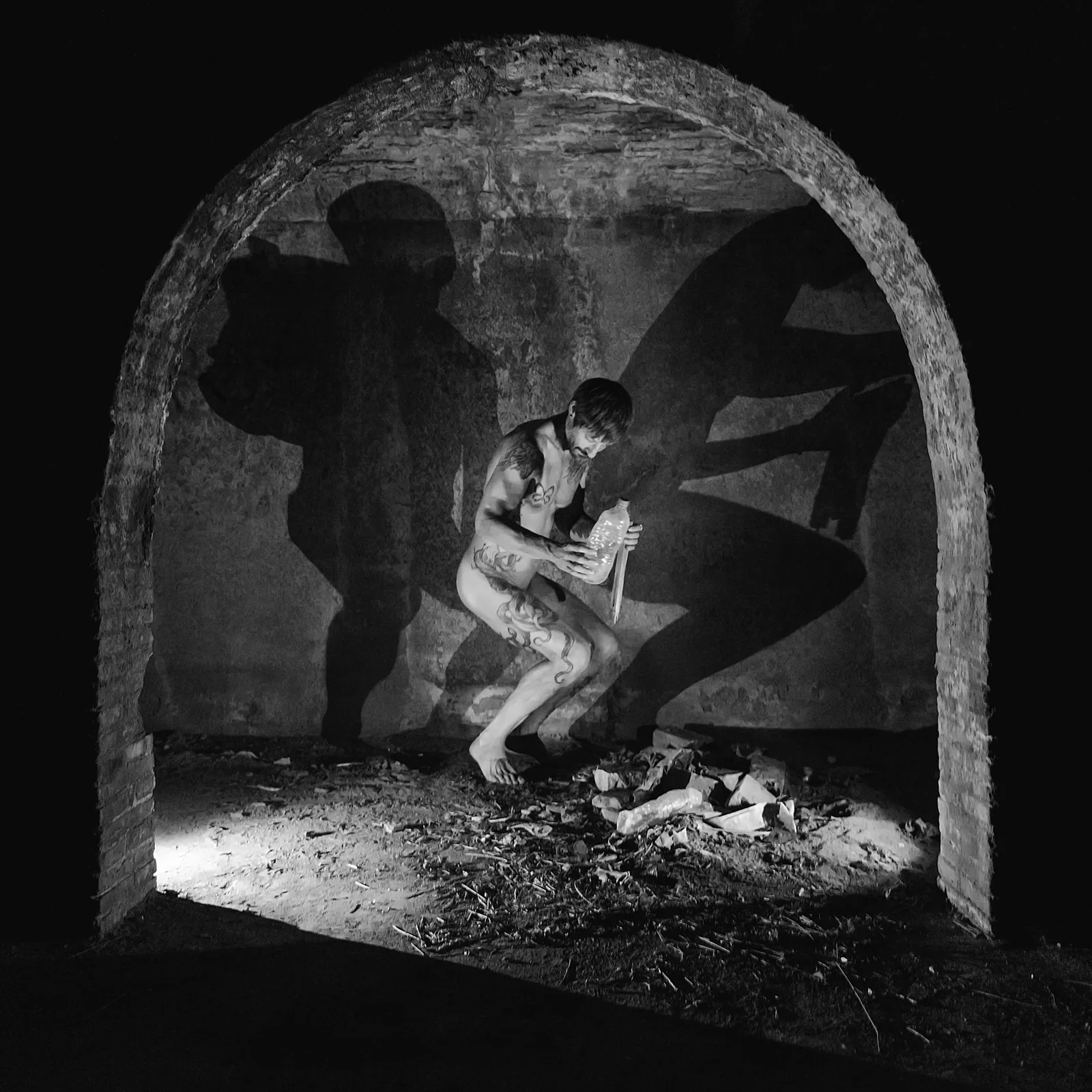 Black-and-white figure crouching among rubble beneath a stone arch.