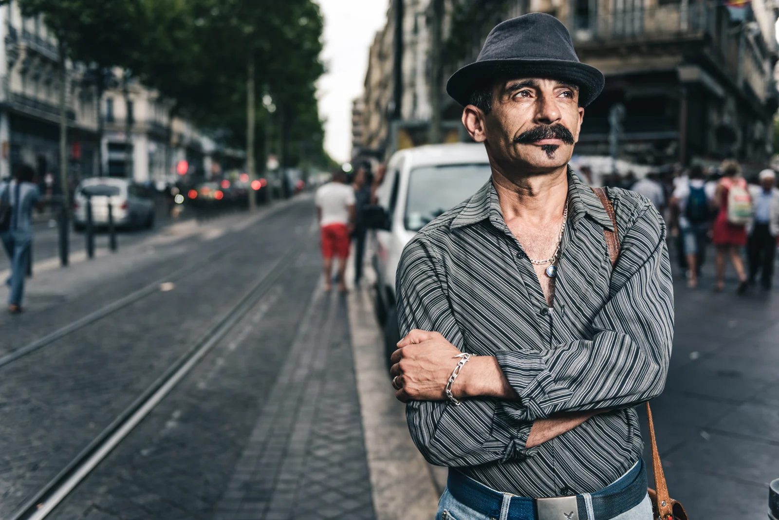 Man with a curled moustache and black hat standing with folded arms.