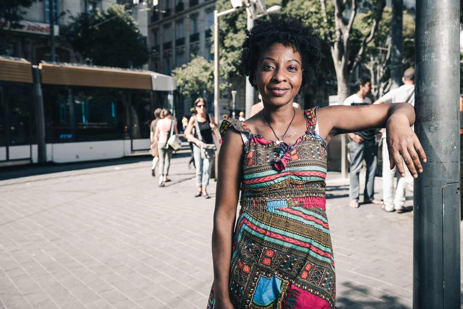 Woman in a striped dress resting an arm on a street post.