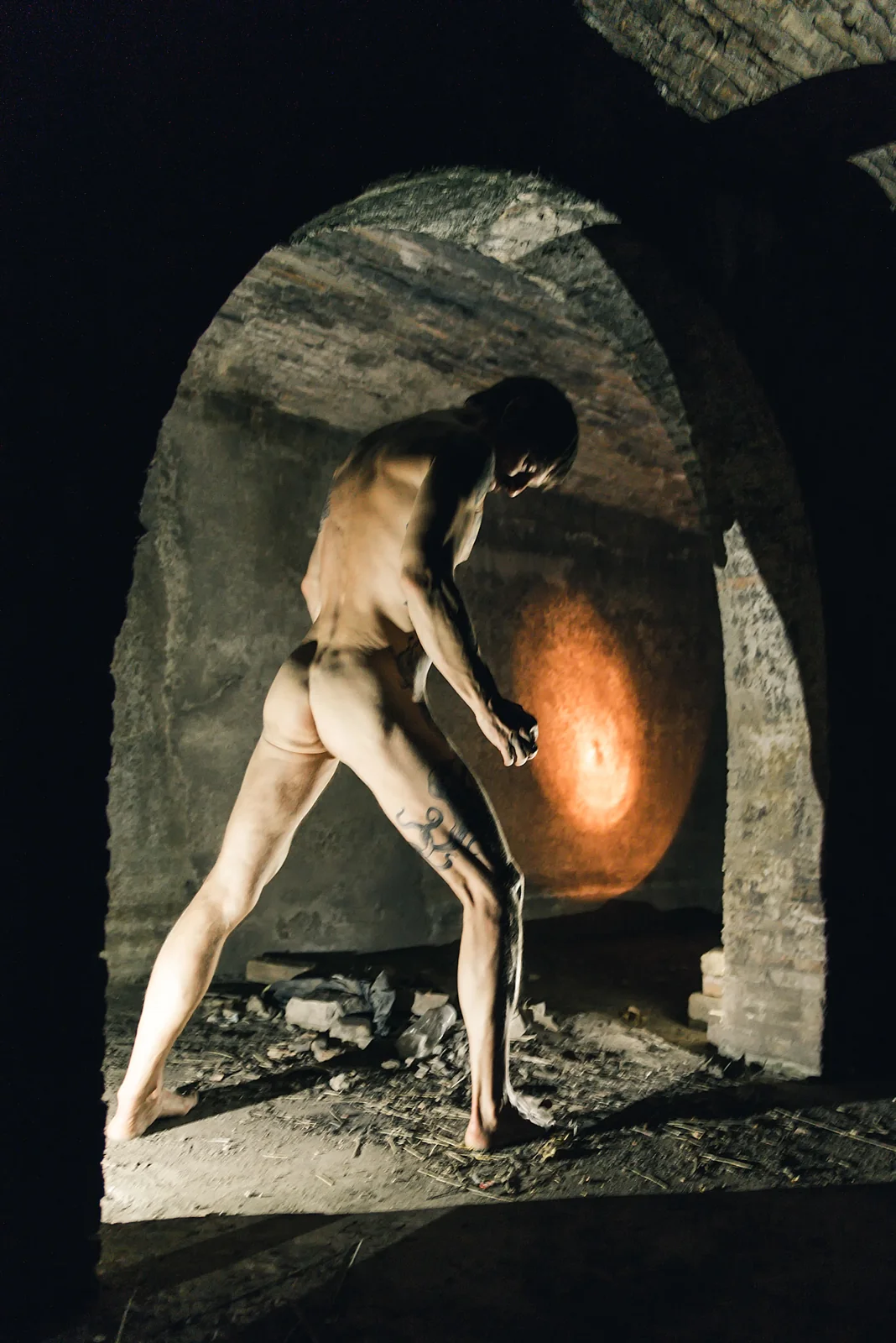 Fine-art nude figure leaning across a stone archway.