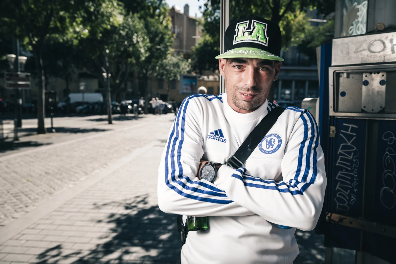 Man in a white football top and green cap leaning beside a doorway.