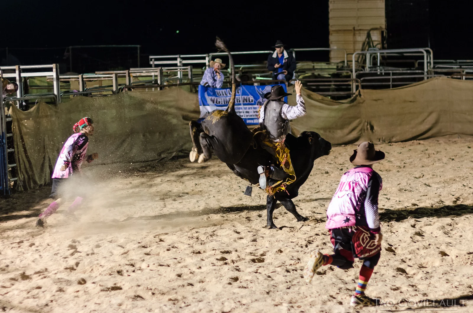 Rider on a bucking bull with arena staff nearby.