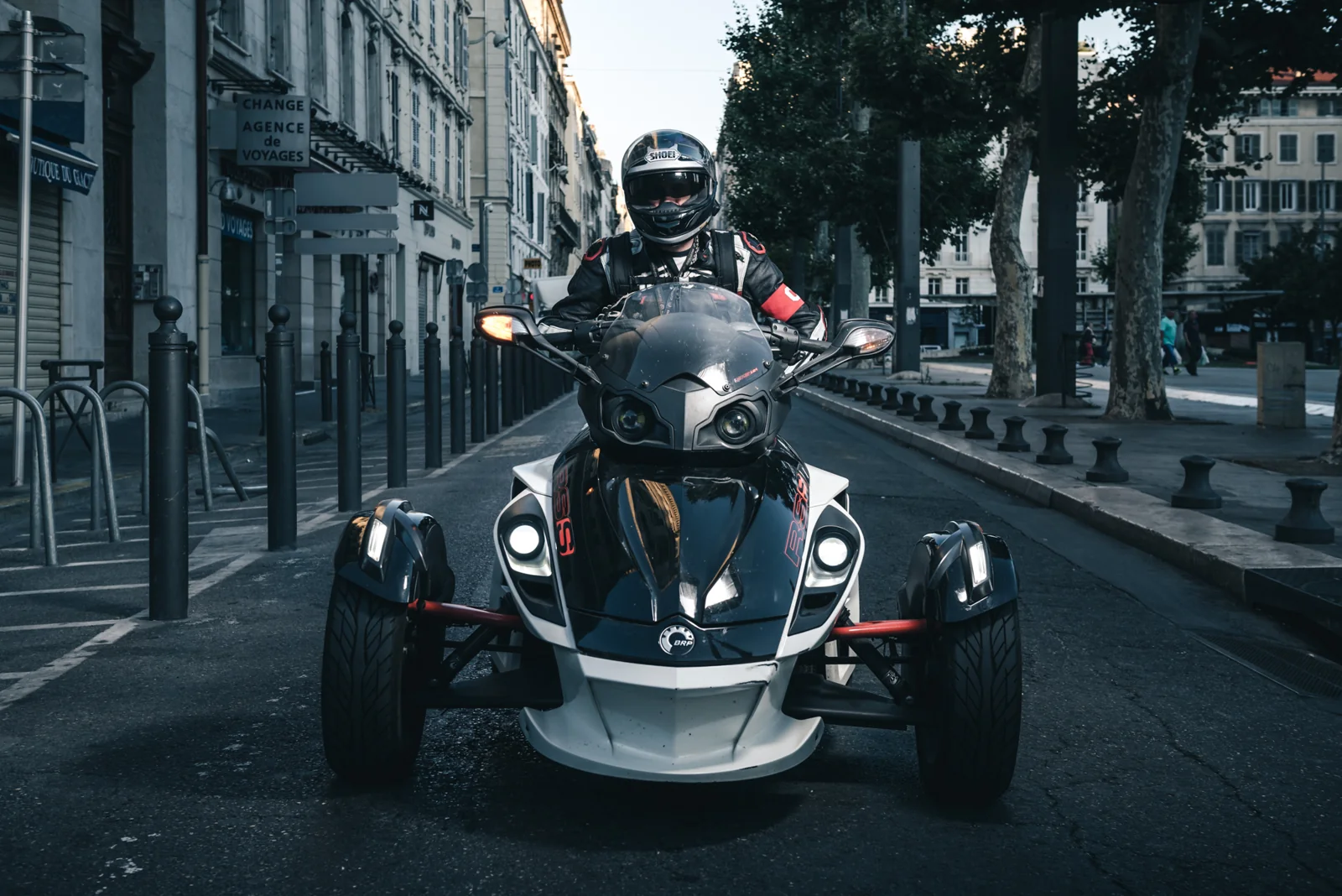 Helmeted rider on a three-wheeled motorcycle in a city street.