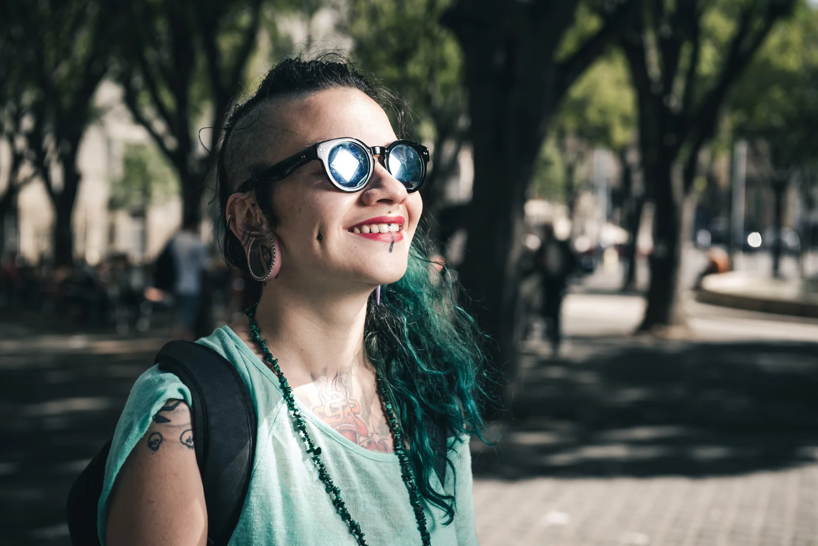 Close portrait of a smiling person with green hair and sunglasses.