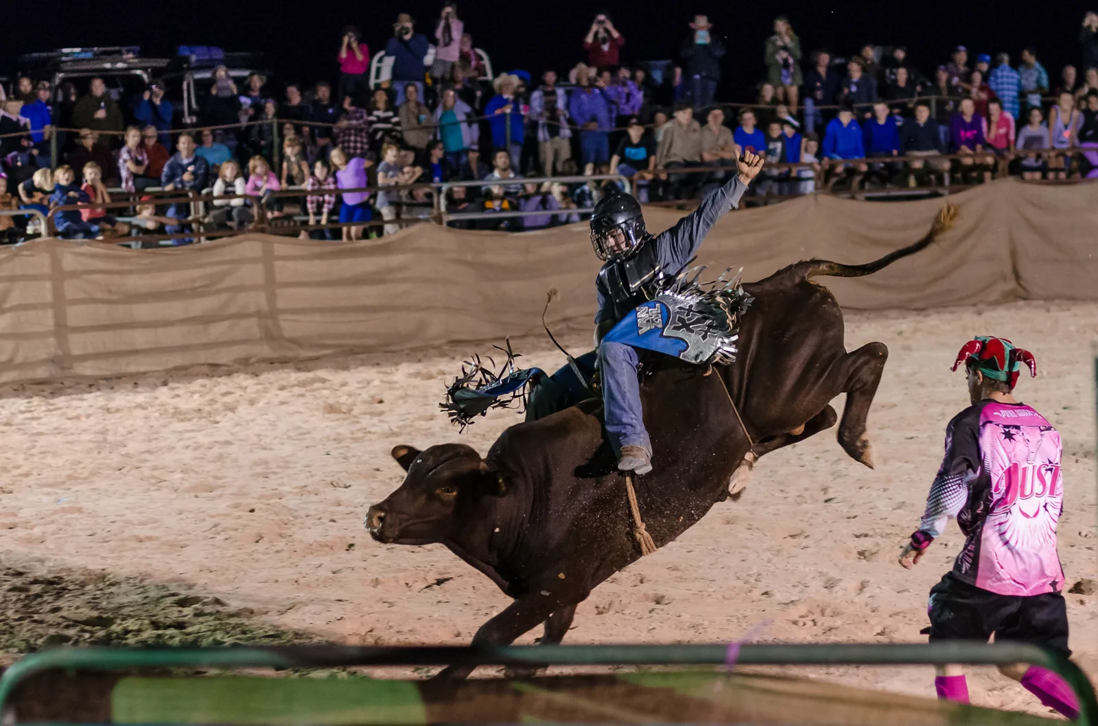 Bull rider competing in a floodlit rodeo arena.