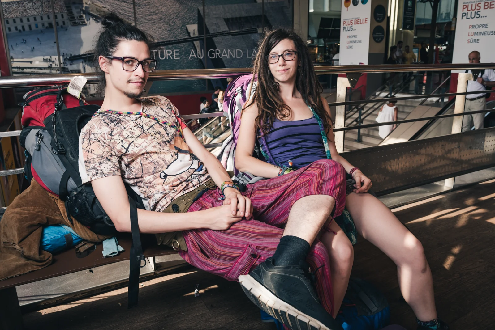 Two people seated together on a bench inside a railway station.