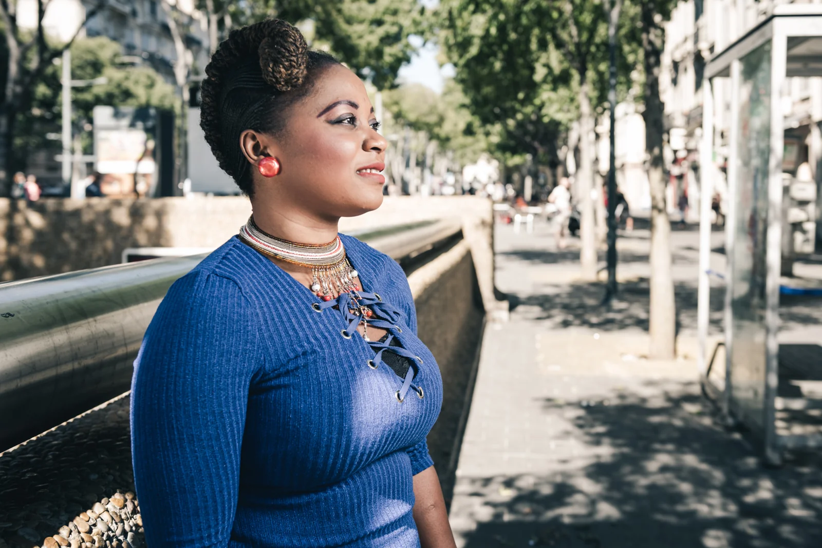 Woman in a blue top standing beside a tree-lined walkway.