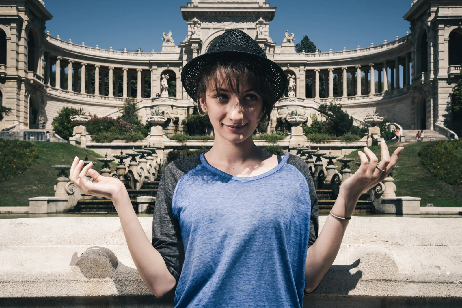 Person in a black hat posing in front of a grand colonnaded fountain.