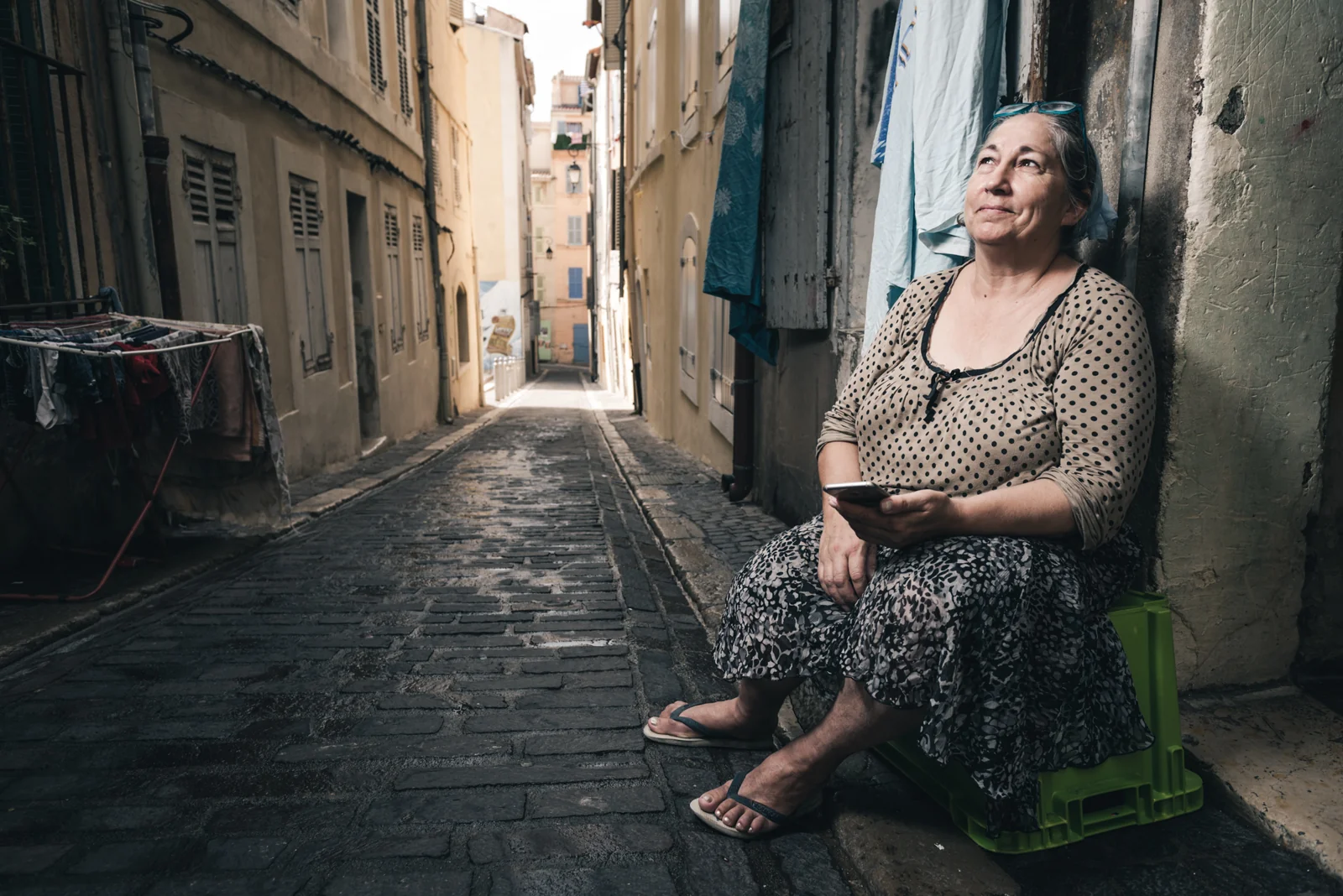 Woman seated on a small chair in a narrow cobbled lane.